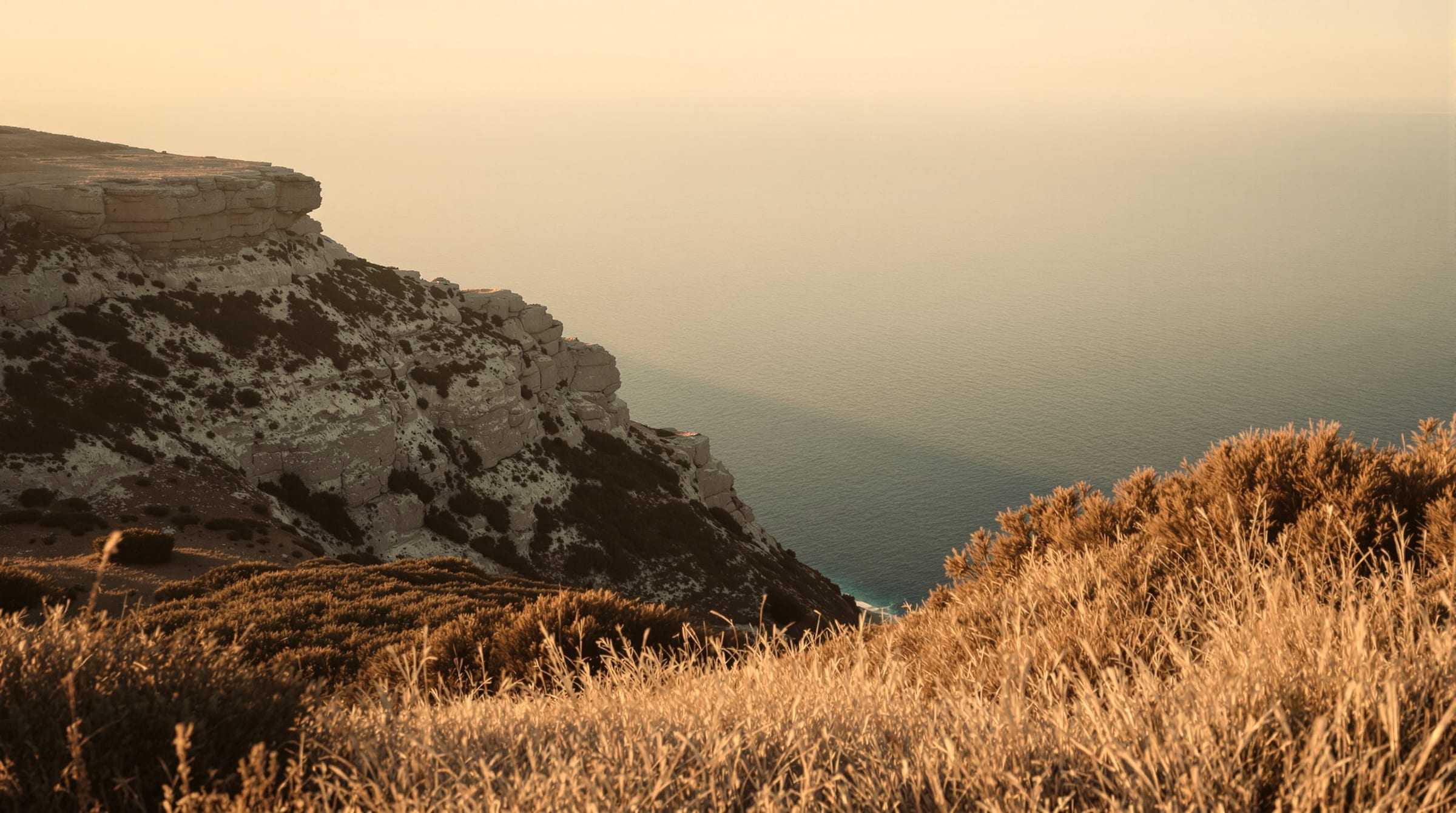 An atmospheric coastal headland at golden hour, layered haze on the horizon, no buildings and no people